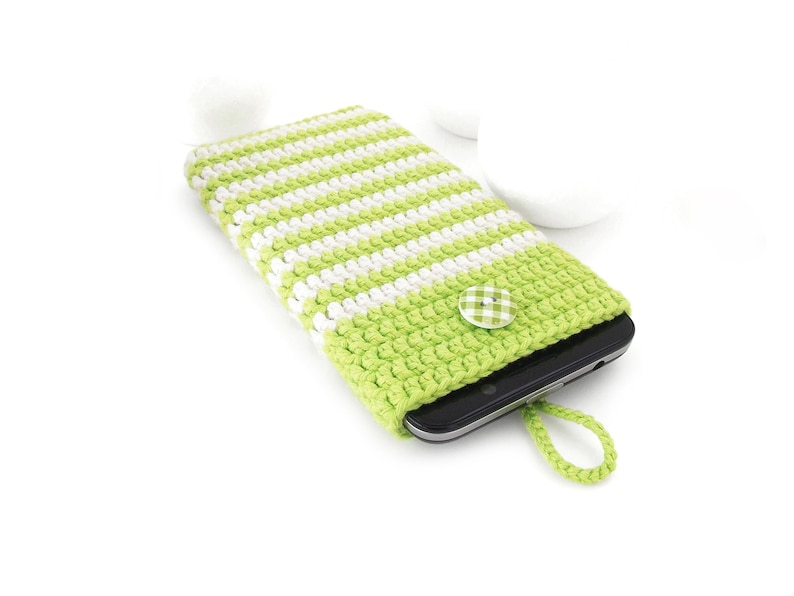 Puede incluir: Una funda de ganchillo para tel&eacute;fono con rayas verde lima y blancas, que presenta una solapa verde lima lisa asegurada por un peque&ntilde;o bot&oacute;n a cuadros verde y blanco. Un lazo trenzado verde lima a juego sobresale de la base de la funda.