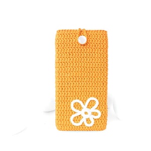 Op de afbeelding: Een gele gehaakte telefoonhoes met een wit gehaakt bloemenmotief en een witte knoopsluiting.