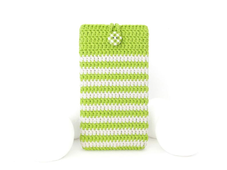 Puede incluir: Una funda de tel&eacute;fono rectangular de ganchillo con rayas horizontales en hilo verde lima y blanco. La funda se asegura en la parte superior con un peque&ntilde;o lazo y un bot&oacute;n redondo decorado con un patr&oacute;n de cuadros vichy blanco y verde.