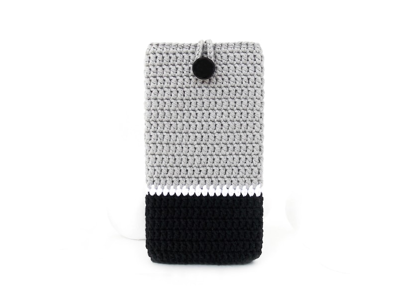 May include: Grey and black crocheted phone case with a white stripe and a black button.