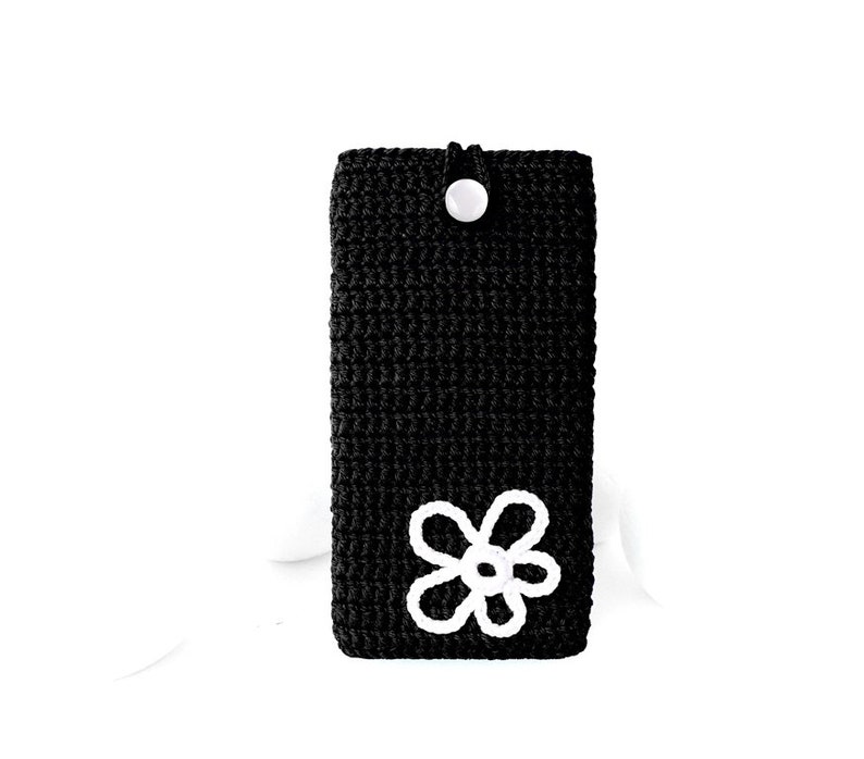 Op de afbeelding: Zwarte gehaakte telefoonhoes met een wit gehaakt bloemenmotief.