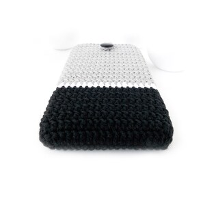 May include: A black and grey crocheted phone case with a button closure.