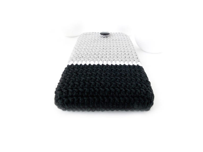 May include: A black and grey crocheted phone case with a button closure.