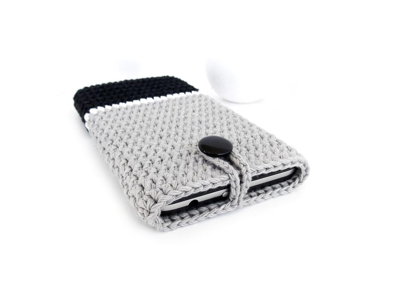May include: Grey, black and white crocheted phone case with a black button closure.
