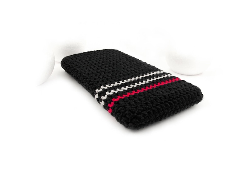 Puede incluir: Funda de tel&eacute;fono de crochet negro con rayas rojas y blancas.