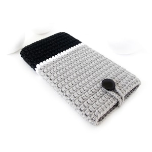 May include: A gray and black crocheted phone case with a white trim and a black button closure.