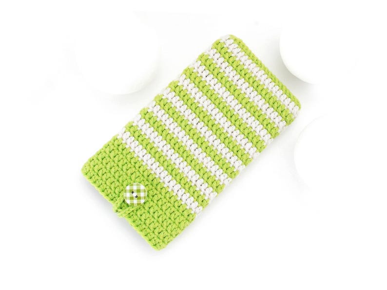 Puede incluir: Una funda rectangular de ganchillo con rayas horizontales alternas de hilo verde lima y blanco. El estuche se asegura con un &uacute;nico bot&oacute;n redondo que presenta un patr&oacute;n de cuadros verde y blanco, situado cerca del borde inferior.