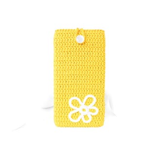 Op de afbeelding: Een gele gehaakte telefoonhoes met een wit gehaakt bloemenmotief en een witte knoopsluiting.
