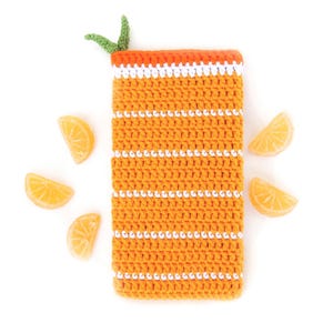 May include: A crocheted orange juice glass with white stripes and a green leaf on top. The glass is surrounded by orange slices.