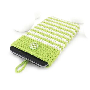 Puede incluir: Una funda de ganchillo para tel&eacute;fono con rayas horizontales de color verde lima y blanco. La funda tiene un peque&ntilde;o lazo verde lima en la parte inferior y se asegura con un bot&oacute;n redondo de cuadros verdes y blancos, conteniendo un m&oacute;vil negro.