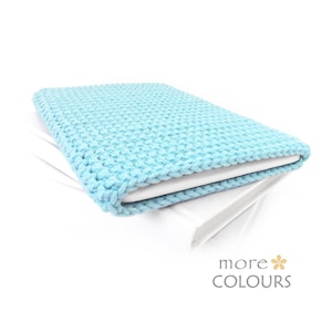 May include: A light blue crocheted laptop sleeve, folded over a white surface. The sleeve is made of a soft, textured yarn.
