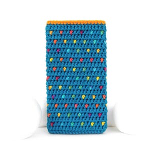 May include: A teal crochet phone case with a colorful dotted pattern. The case has an orange border and is made of a soft, textured yarn. The colorful dots are in shades of red, yellow, blue, and green.