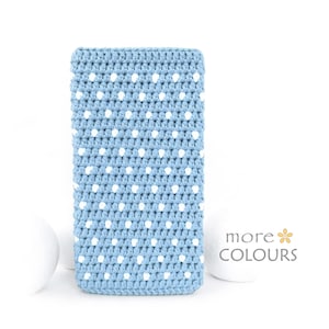 May include: A light blue, rectangular crochet case with white polka dots. The case is handmade and has a textured appearance. The words "more COLOURS" are visible in the lower right corner. The case is likely designed to hold a phone or other small device.