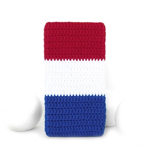 Puede incluir: Un objeto rectangular de ganchillo en rojo, blanco y azul, que se asemeja a una bandera. La sección superior es roja, el medio es blanco y la parte inferior es azul. El artículo es probablemente una funda de teléfono o una pequeña bolsa.