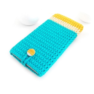 May include: A turquoise crochet phone case with a yellow and cream-colored top section. The case is secured with a matching turquoise loop and a yellow button. The handmade case is on a white background.
