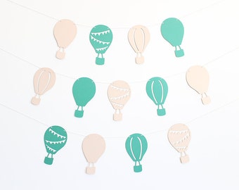 Puede incluir: Una guirnalda de globos de aire caliente de papel en colores azul verdoso y beige. Los globos están unidos con una cuerda blanca.