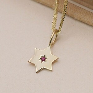 May include: A gold chain necklace with a star of David pendant featuring a small red gemstone in the center.