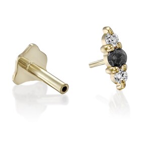 May include: A gold earring with a black diamond and two white diamonds. The earring is set in a curved shape with a small gold post.