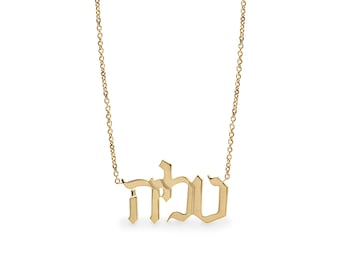 May include: Gold necklace with a Hebrew word pendant in a gothic font. The word is "שלום" which means "peace" in English.