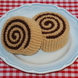 May include: Two crocheted cinnamon rolls on a blue and white plate. The rolls are brown and tan with a swirl pattern.