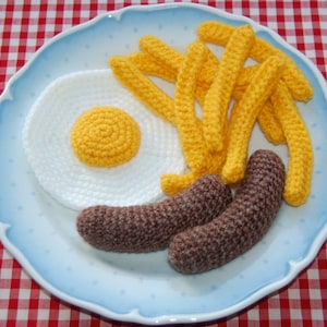May include: A blue plate with a crocheted breakfast of two brown sausages, a white egg with a yellow yolk, and yellow chips.