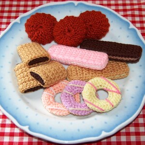 May include: A blue plate with crocheted food items, including doughnuts, biscuits, and cookies. The plate is on a red and white checked tablecloth.