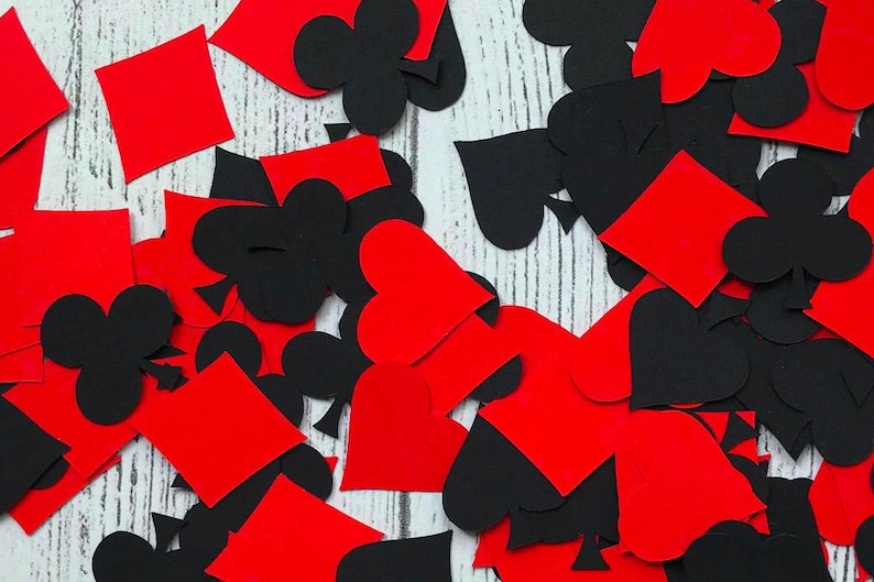 Puede incluir: Recortes de papel rojo y negro de palos de cartas de juego, incluyendo corazones, diamantes, picas y tr&eacute;boles. Los recortes est&aacute;n esparcidos sobre una superficie de madera blanca.