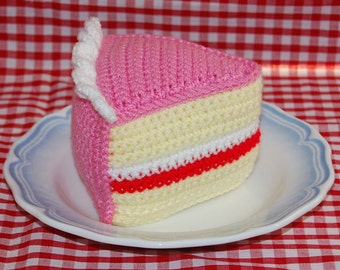 May include: A crocheted pink and white cake slice with a white frosting and red filling. The cake slice is on a white plate with a blue rim.