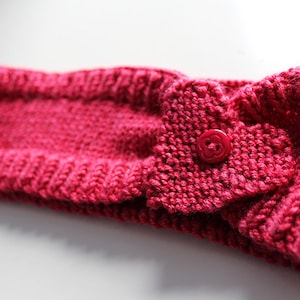 Puede incluir: Una diadema de punto rosa con un detalle en forma de corazón y un botón rojo.