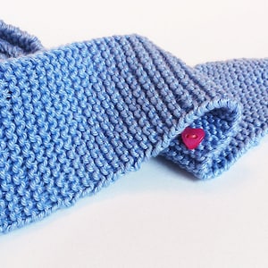 Puede incluir: Una bufanda de punto azul claro con un botón rosa en forma de corazón.