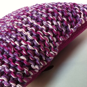 Puede incluir: Primer plano de una almohada de punto de ganchillo de color morado, blanco y lavanda con cierre de cremallera.