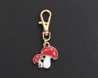 May include: A gold-colored keychain with a red and white mushroom charm. The mushroom has white spots and a small stem.