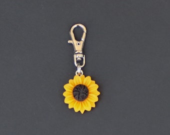 May include: A silver keychain with a yellow sunflower charm. The sunflower has a black center.