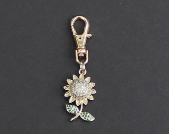 May include: A gold-tone keychain featuring a sunflower with green leaves and a gold-tone clasp.