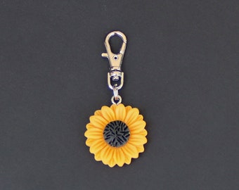 May include: A silver keychain with a yellow sunflower charm. The sunflower has a black center.