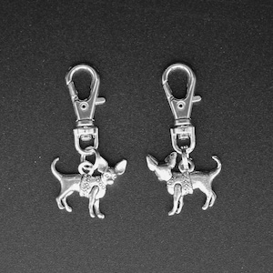 May include: Two silver keychains with small silver chihuahua charms. The charms are wearing sweaters.