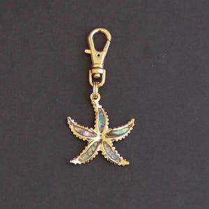 May include: A gold-tone keychain with a  starfish charm. The starfish is made of iridescent abalone shell.