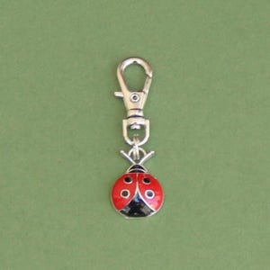 May include: A silver-toned metal clip-on charm featuring a red ladybug design with black spots and a black head. The ladybug charm is attached to a lobster clasp for easy attachment to a keychain or bag.