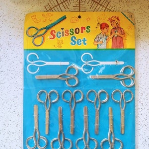May include: A package of 10 small silver scissors on a blue background. The package is yellow and features a cartoon illustration of children using scissors. The text on the package reads "Scissors Set".