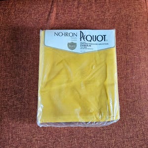 May include: A packaged yellow flat sheet from Pequot. The sheet is labeled "No-Iron" and "luxury muslin." The packaging also indicates the sheet is a twin flat size, measuring 72 x 104 inches, made of 50% polyester and 50% cotton.