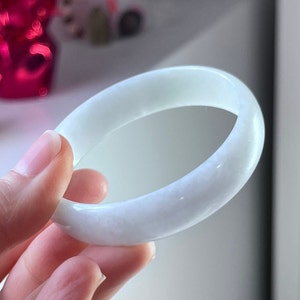 May include: A white jade bangle bracelet. The bracelet is smooth and polished, with a subtle sheen.