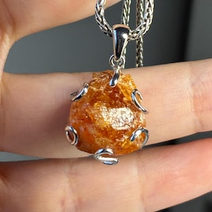May include: A silver chain necklace with a pendant featuring a large, rough, orange-brown gemstone set in a silver wire cage.
