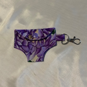 May include: Purple floral fabric key chain with a small pocket and a silver metal clasp.
