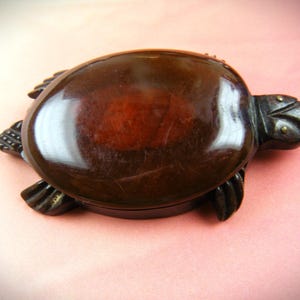May include: A dark brown turtle-shaped trinket box with a glossy finish. The box is made of wood and has a detailed carving of a turtle's head and legs.