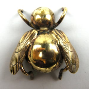 Könnte beinhalten: Eine goldfarbene Metall-Bienenbrosche mit detaillierten Flügeln. Die Biene ist ein beliebtes Insektenmotiv in Schmuck.