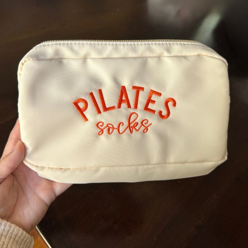 May include: A white zippered pouch with the text "PILATES socks" embroidered in orange.