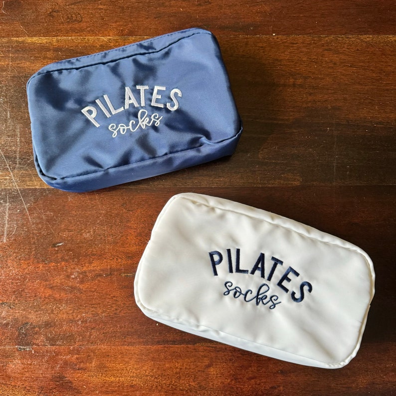 May include: Two white fabric pouches with blue embroidery that reads "PILATES socks".