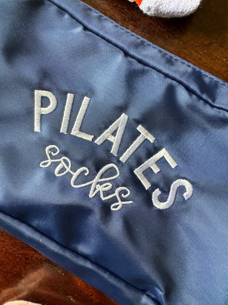 May include: A navy blue zippered pouch with white embroidery that reads "PILATES socks".