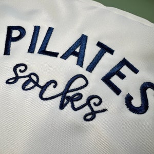 May include: White fabric bag with the text "PILATES socks" embroidered in navy blue.