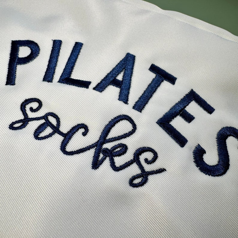 May include: White fabric bag with the text "PILATES socks" embroidered in navy blue.